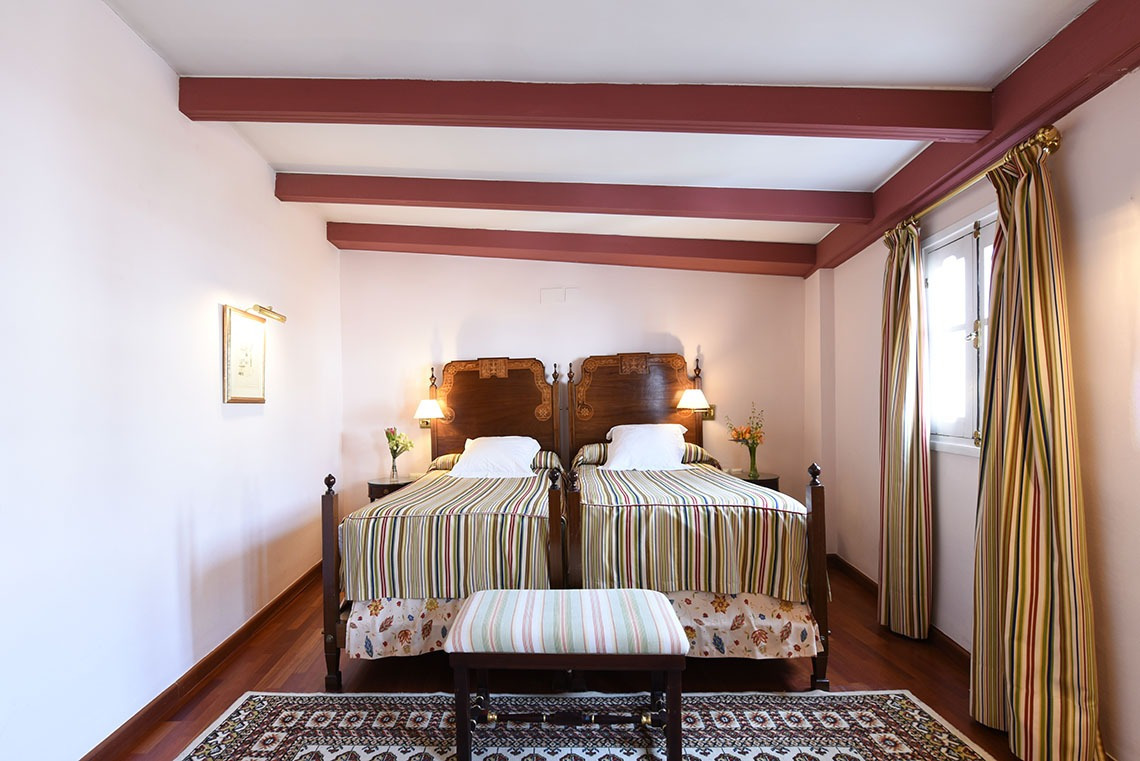 A twin room with two separate beds, wooden beams and warm lamplight