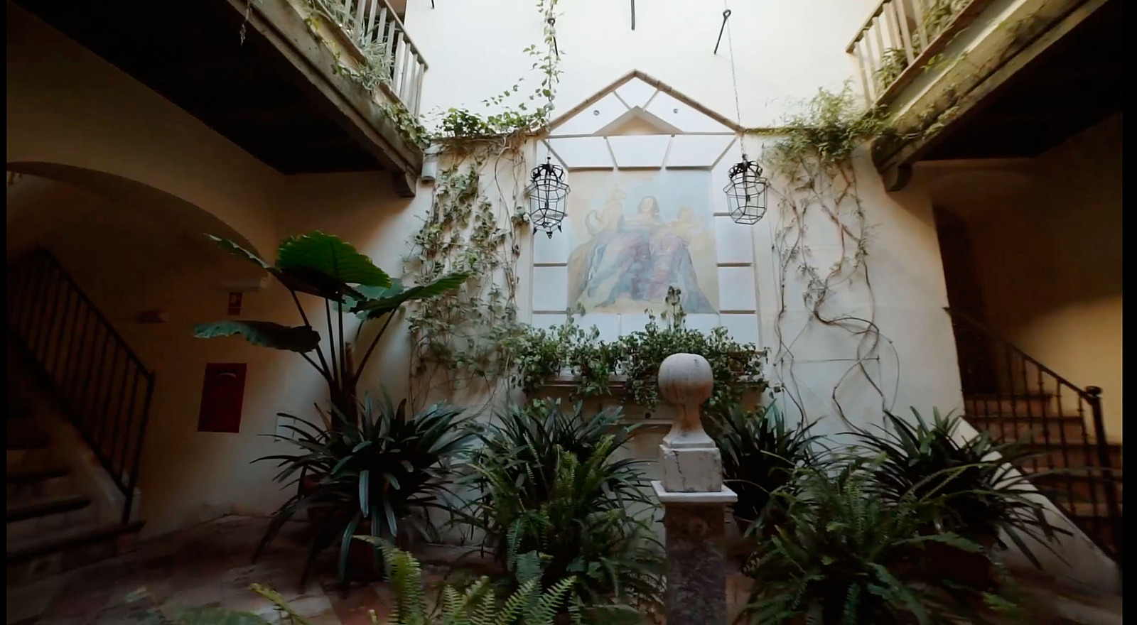 A plant-filled interior patio with arches and a stone fountain
