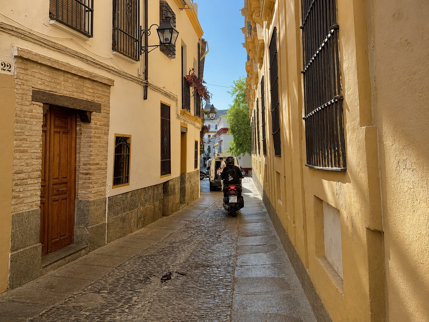 A sunlit narrow cobbled street in Seville's old quarter with ochre walls and wrought-iron lanterns